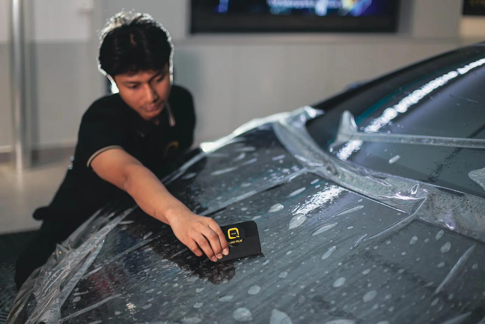 Technician squeegeeing paint protection film across a black car's bonnet