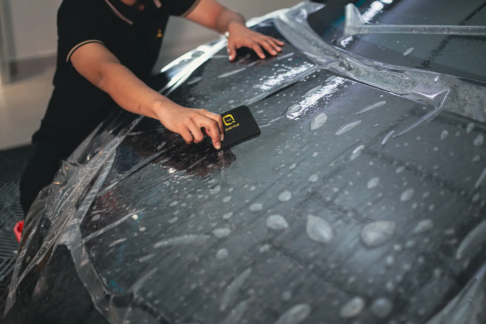 BMW iX3 PPF Malaysia reference shot of a technician squeegeeing paint protection film across a wet black car panel
