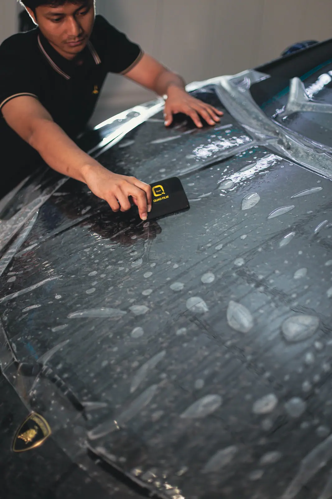 A wet squeegee pass across a dark panel, the stage where a Jaecoo J7 window tint job either flushes the dust out or traps it.