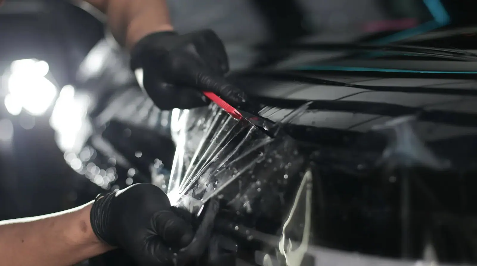 Clear paint protection film being hand-trimmed beside a dark car panel edge