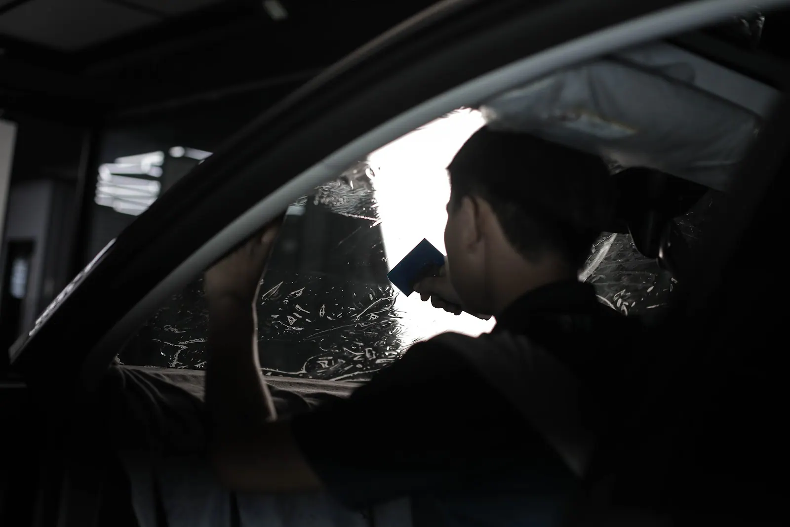 Technician squeegeeing wet window tint against the inside of a car side window.